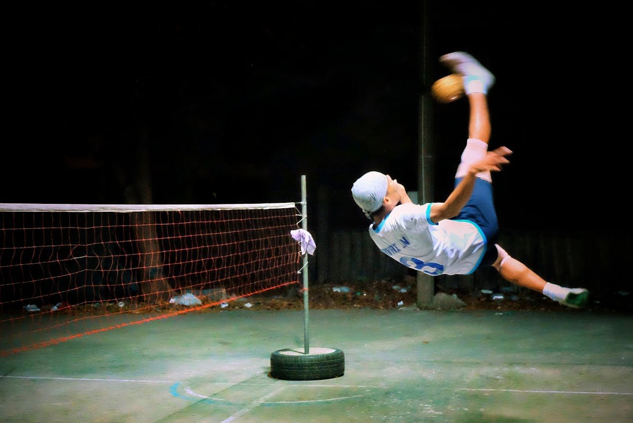 A player performs an acrobatic kick in a nighttime Sepak Takraw match.
